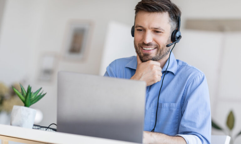 Hotline Support Service. Male call center operator in headset working with laptop Hotline Support Service. Handsome male call center operator in headset working with laptop in modern office, looking at computer screen, free space